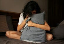 현대인의 불면증: 원인과 해결책 A woman sitting on a bed holding a pillow