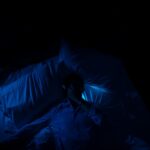 “10분만 더 누워있을까?” 아침 피로의 진짜 원인, ‘수면 빚’ 때문입니다 A person laying in a bed in a dark room