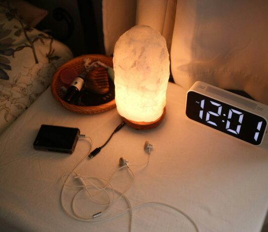 “슬립테크”와 함께 깊은 잠에 빠지다…수면 건강 관리법 Nightstand with a lamp, clock, and chargers.