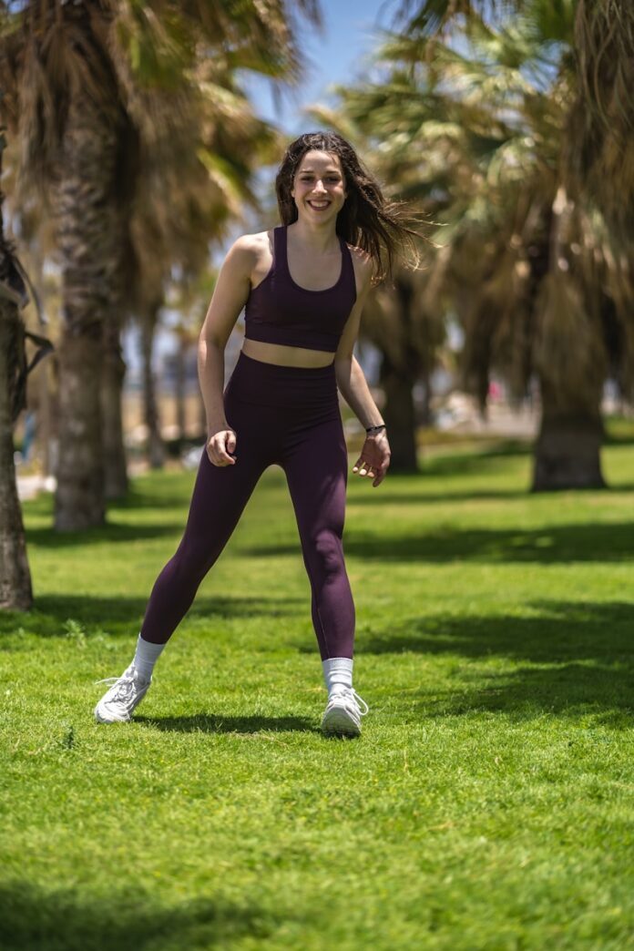 woman in black tank top and purple leggings running on green grass field during daytime