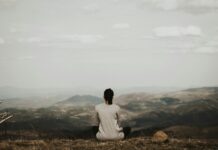 “만성피로, 단순한 피곤함이 아니다…AI 수면관리·‘마인드풀니스’로 해법 찾는다” woman sitting on cliff overlooking mountains during daytime