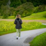 일상 속 ‘마음 챙김 걷기’, 스트레스 관리와 건강 두 마리 토끼 잡는다 Woman walking on a winding road through fields.