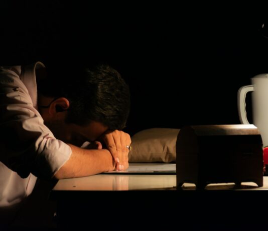감정 억압이 위장과 흉부에 쌓이는 신체 감각의 정체 Man resting head on desk in dark room