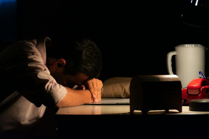 Photo by Human Bahluli Man resting head on desk in dark room