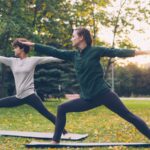 “벽을 넘어 숲으로”… 마음의 병 치유하는 ‘그린 엑서사이즈’ 열풍 Two women practicing yoga warrior pose outdoors.