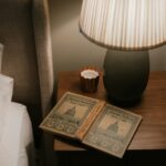 바쁜 일상 속, ‘수면 루틴’이 건강 트렌드로…실생활 적용 팁은? Open book on bedside table with lamp
