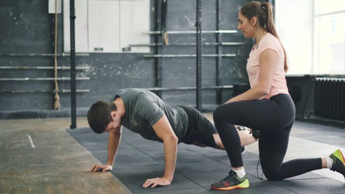 Man doing push-ups with a trainer spotting him.