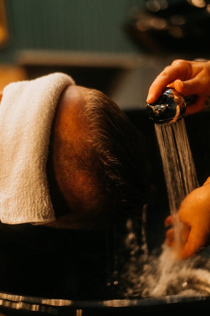 Photo by Redd Francisco a man getting his hair washed in a sink