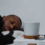 잠들기 전 루틴이 바뀐다…수면 건강 지키는 신(新) 트렌드와 실천법 a man sleeping on top of a stack of books next to a cup of coffee