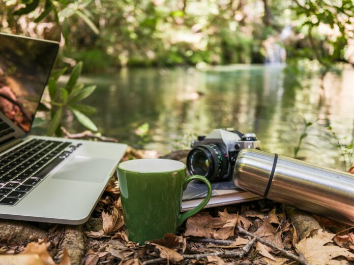 Laptop, camera, and mug by a forest stream