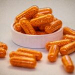 나에게 맞는 영양제, 어떻게 고를까?—최근 트렌드와 실생활 팁 Orange capsules filled with small beads spill from container.