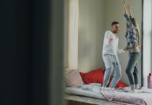 층간소음 걱정 없는 ‘방구석 댄스’ 홈트레이닝 꿀팁 Couple dancing joyfully on a bed near window.