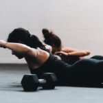 필라테스 열풍, 현대인의 몸과 마음을 바꾼다…집에서 시작하는 생활 속 필라테스 루틴 woman in black tank top and black leggings lying on black floor