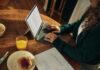 일상 속 정신건강, 작은 변화가 주는 큰 힘 Woman typing on laptop at wooden table with breakfast.