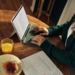 일상 속 정신건강, 작은 변화가 주는 큰 힘 Woman typing on laptop at wooden table with breakfast.