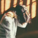 만성피로, 단순한 피로 아냐…지속되면 질병 신호일 수 있다 woman leans on wall in white fur jacket docking her head while holding it using her leaf hand