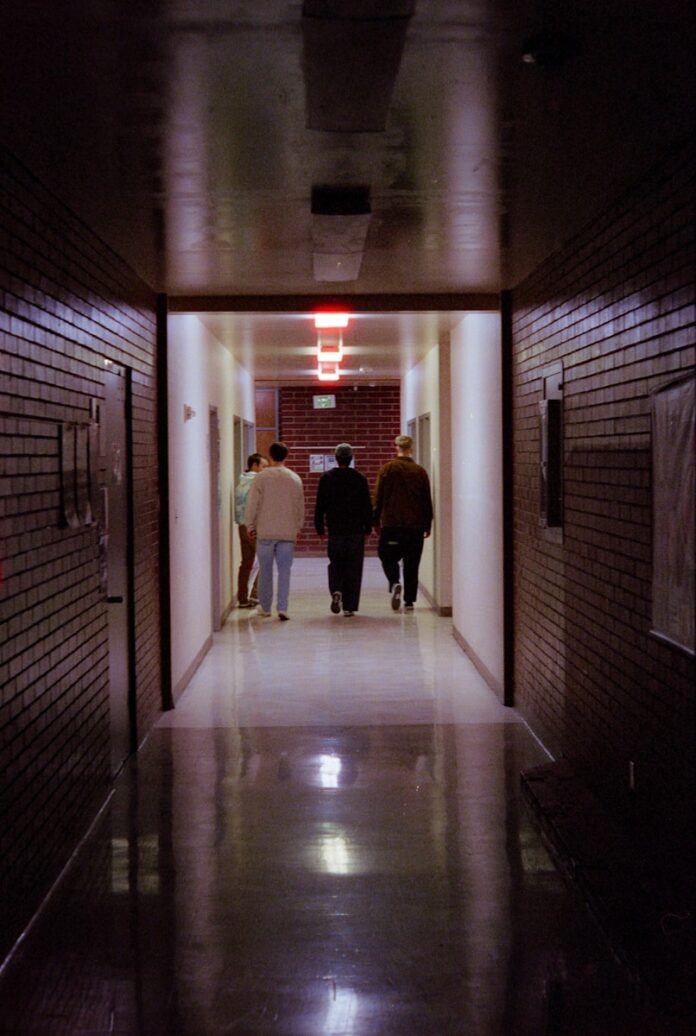 Photo by Spencer Plouzek People walk down a dark, brick-walled hallway.