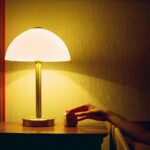 집에서 쉽게 실천하는 ‘스마트한 수면 루틴’이 주목받는다 a person's hand on a table next to a lamp