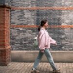 일상 속 걷기, 건강을 지키는 가장 손쉬운 비결 A woman walks along a brick wall.