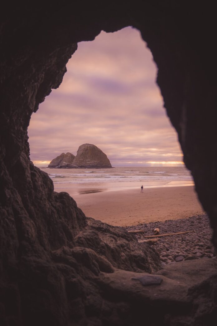 Photo by Sharad Bhat Sea stack and beach visible through a dark cave opening.