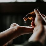 ‘슬기로운 헤어케어’… 건강한 모발을 위한 일상 속 실천법 person holding amber glass bottle