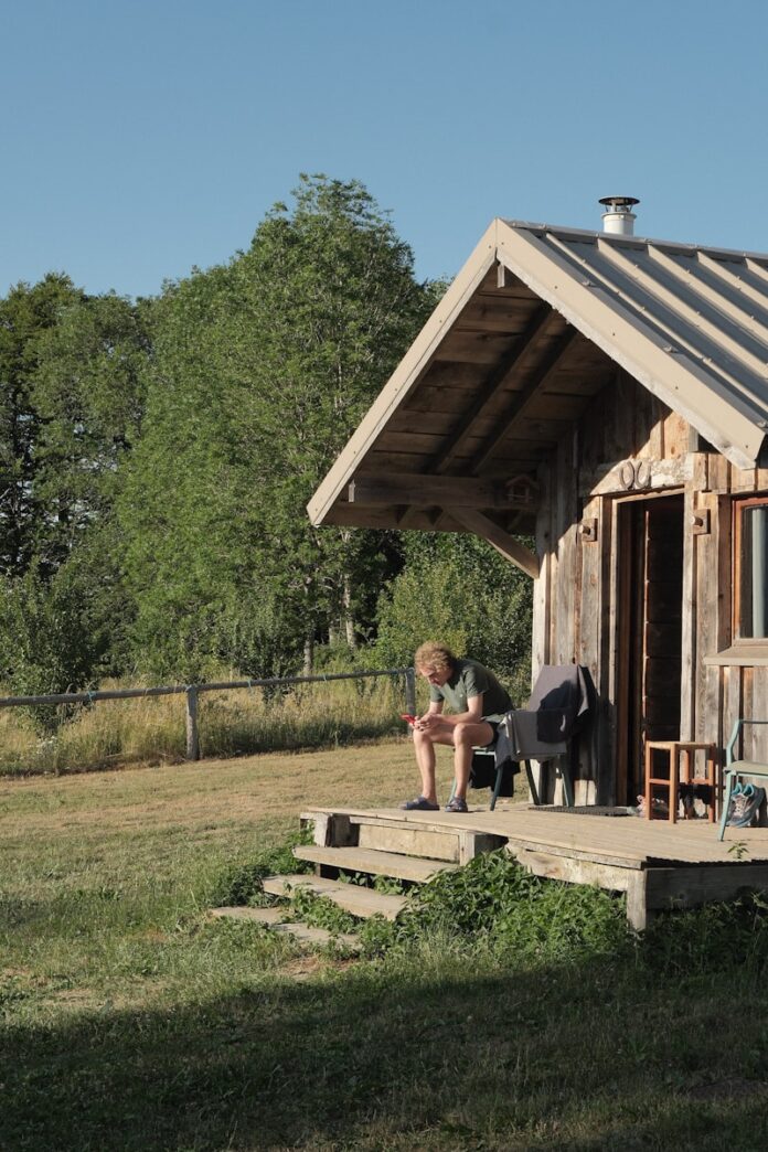 Photo by Rosalie Gdy Man sitting on rustic cabin porch in nature.