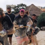 소셜 크루 액티비티의 건강한 매력, 함께하는 즐거움과 웰빙을 누리자! Men playing tug-of-war on a sandy beach