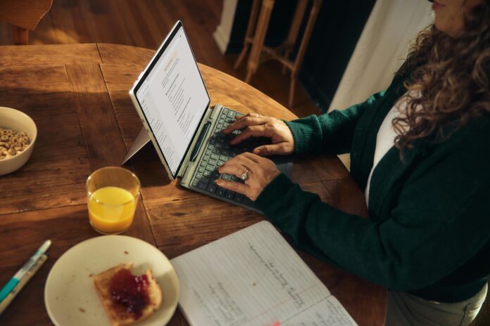 Photo by Microsoft Copilot Woman typing on laptop at wooden table with breakfast.