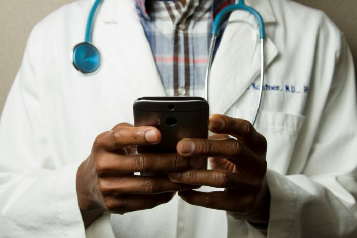 Photo by National Cancer Institute person wearing lavatory gown with green stethoscope on neck using phone while standing