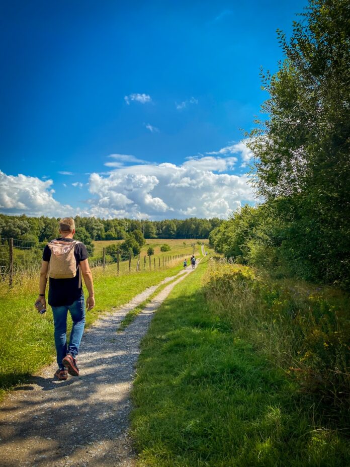 Photo by Jennifer Latuperisa-Andresen man in brown t-shirt and blue denim shorts walking on pathway between green grass field