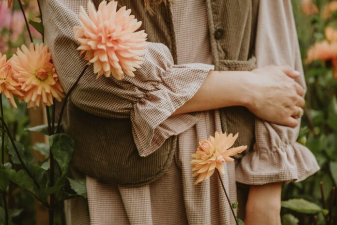 Photo by Anita Austvika A person in a brown gingham dress and corduroy vest among peach dahlias