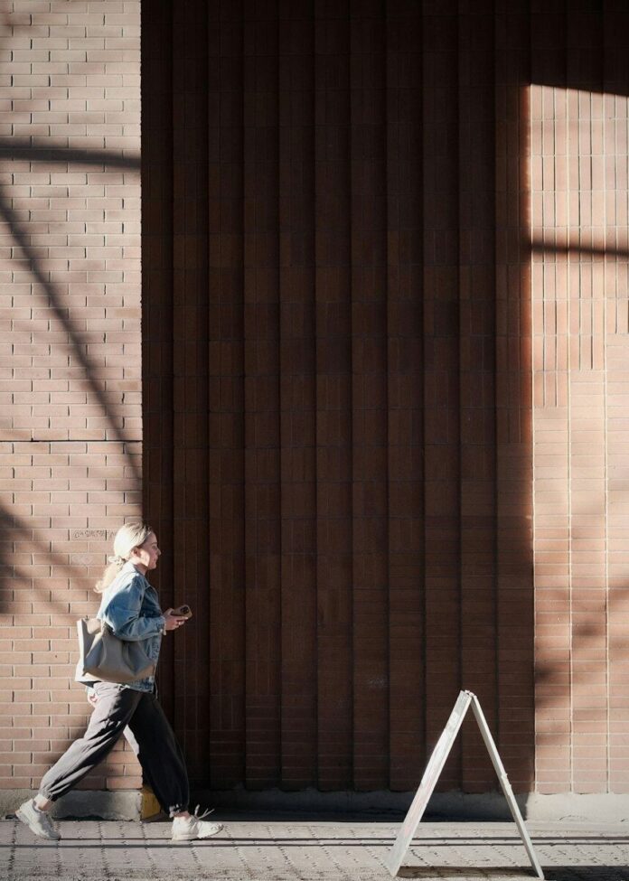 Photo by Kris Tian Woman walking past a brick building with shadows
